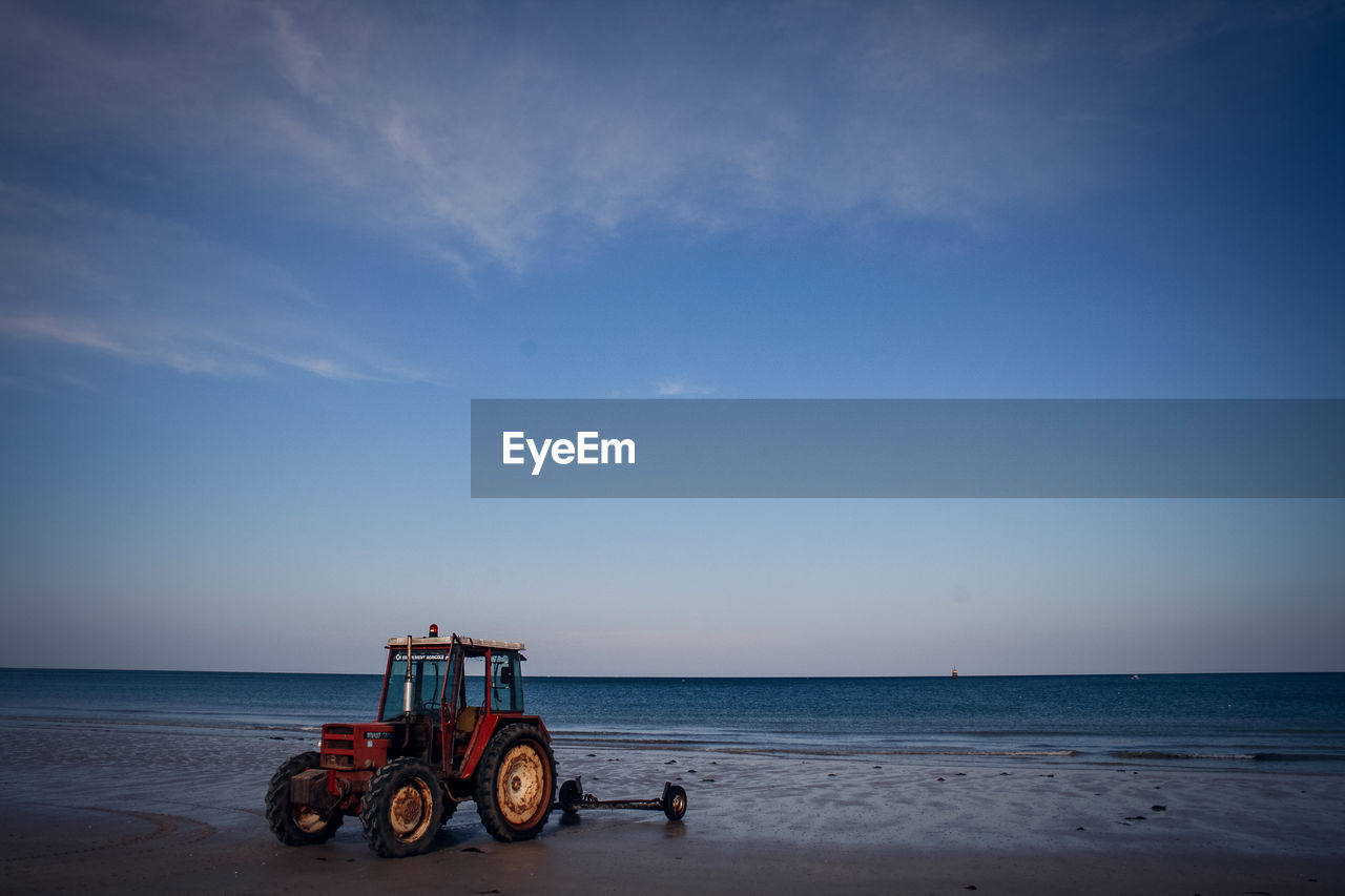 Tractor on shore at beach against sky