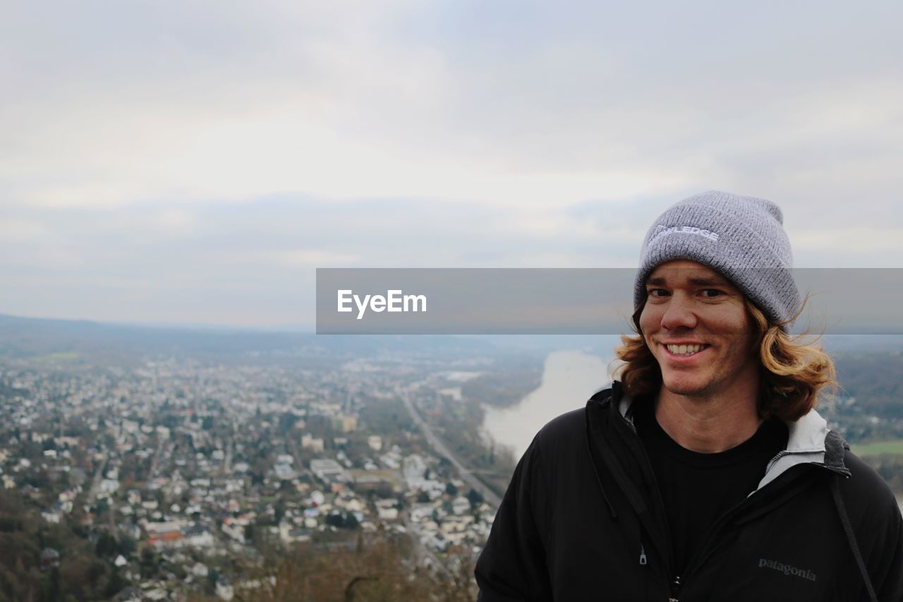 PORTRAIT OF SMILING YOUNG MAN STANDING AGAINST SKY