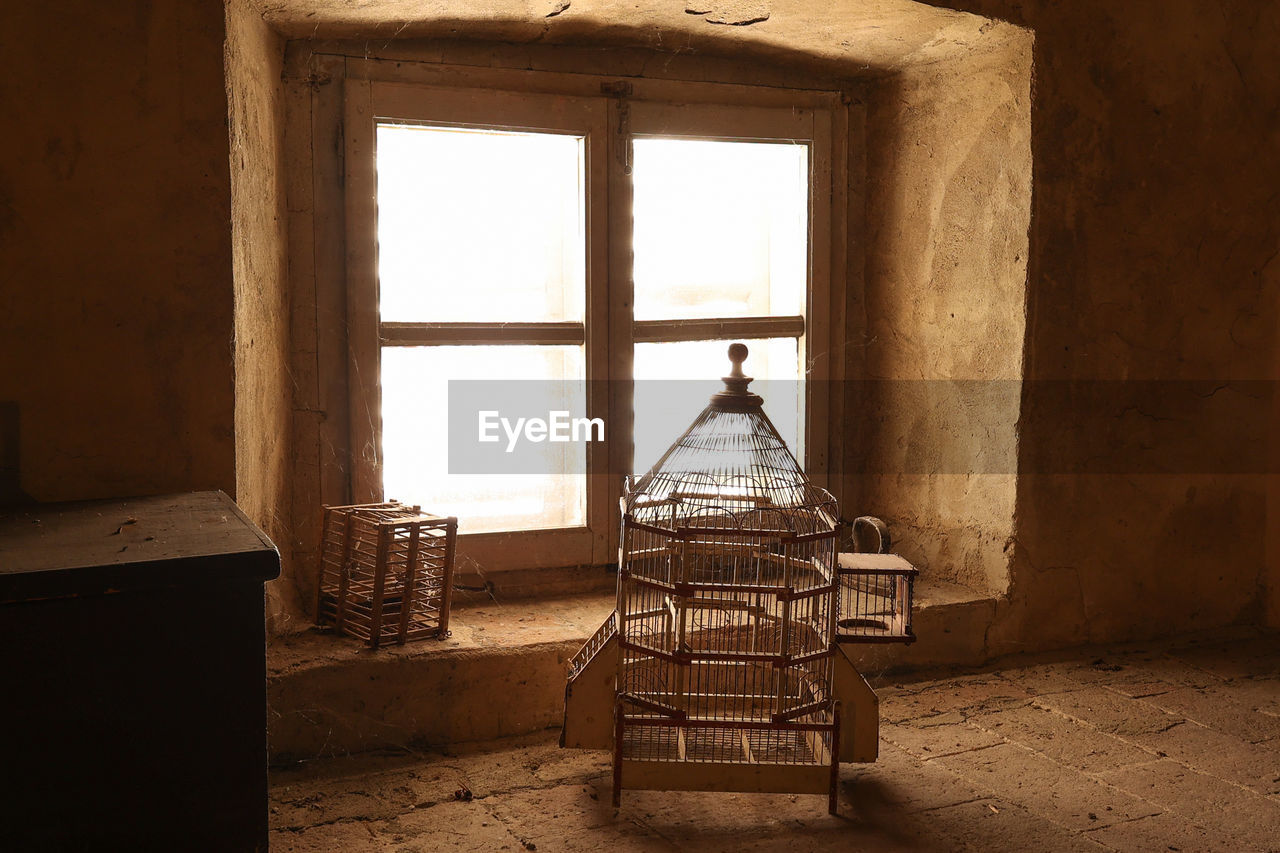 Two empty old wooden bird cages in a attic in front of a window 