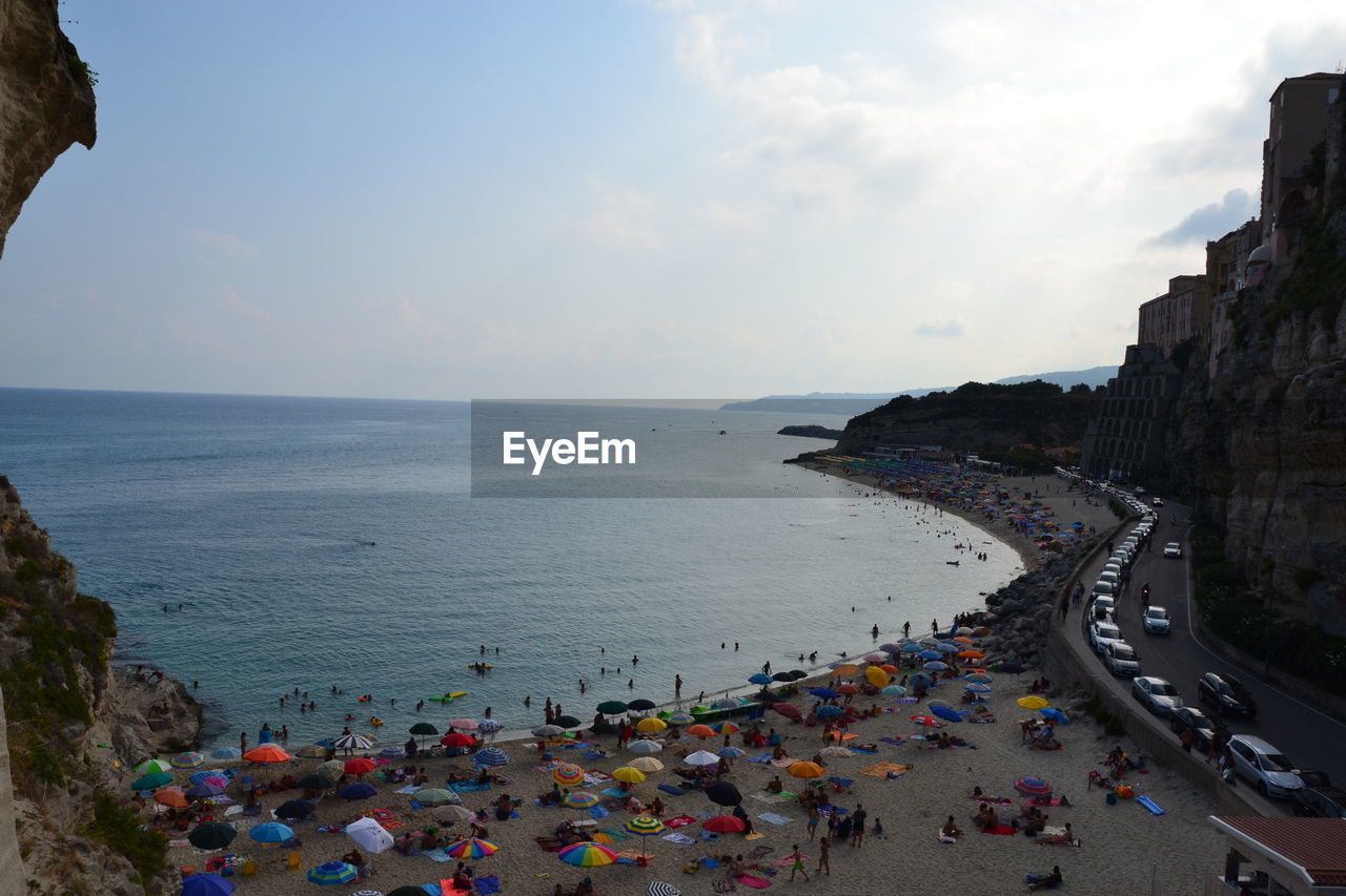 HIGH ANGLE VIEW OF CROWD AT BEACH AGAINST SKY