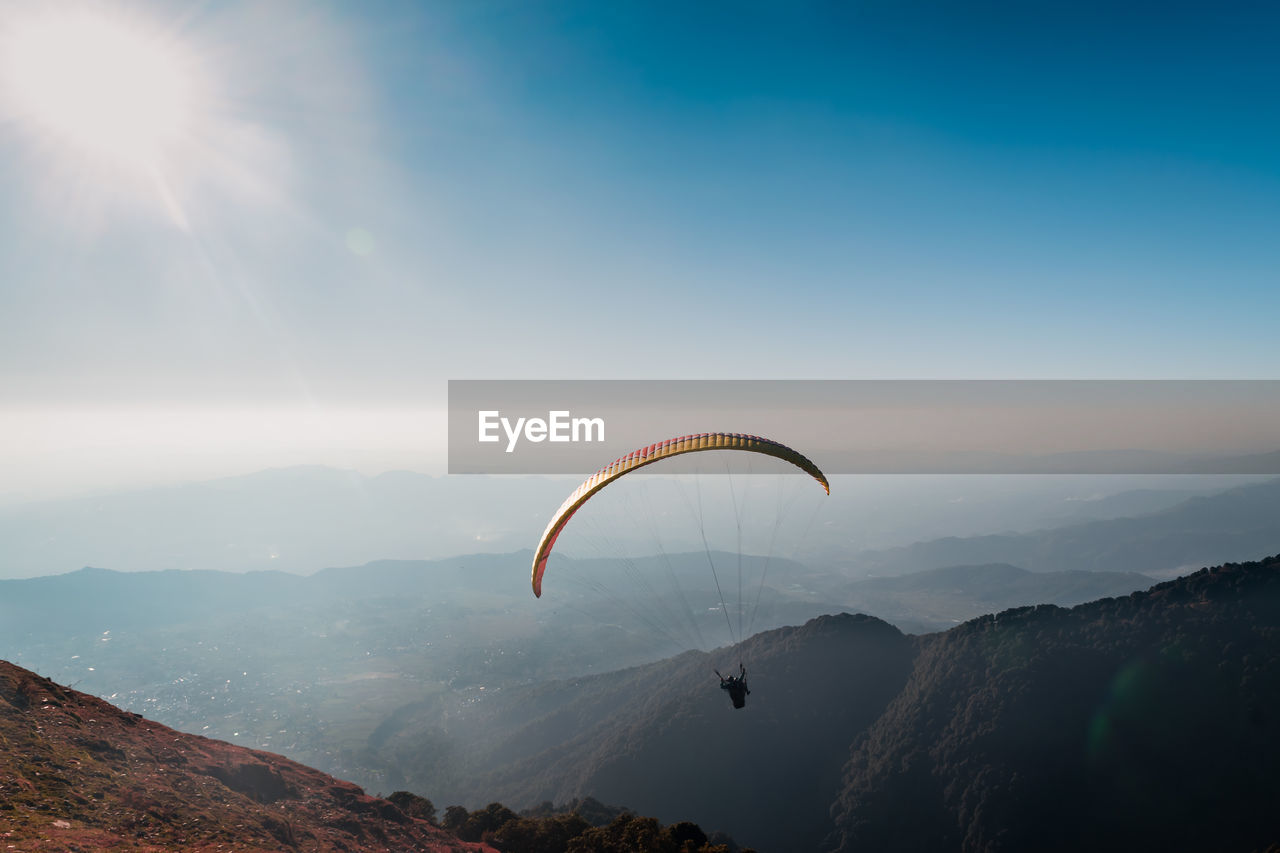 Person paragliding over mountains against sky