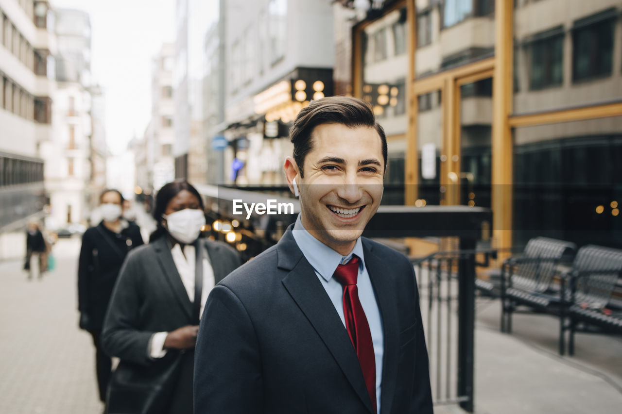 Happy businessman social distancing with female colleagues on street in city