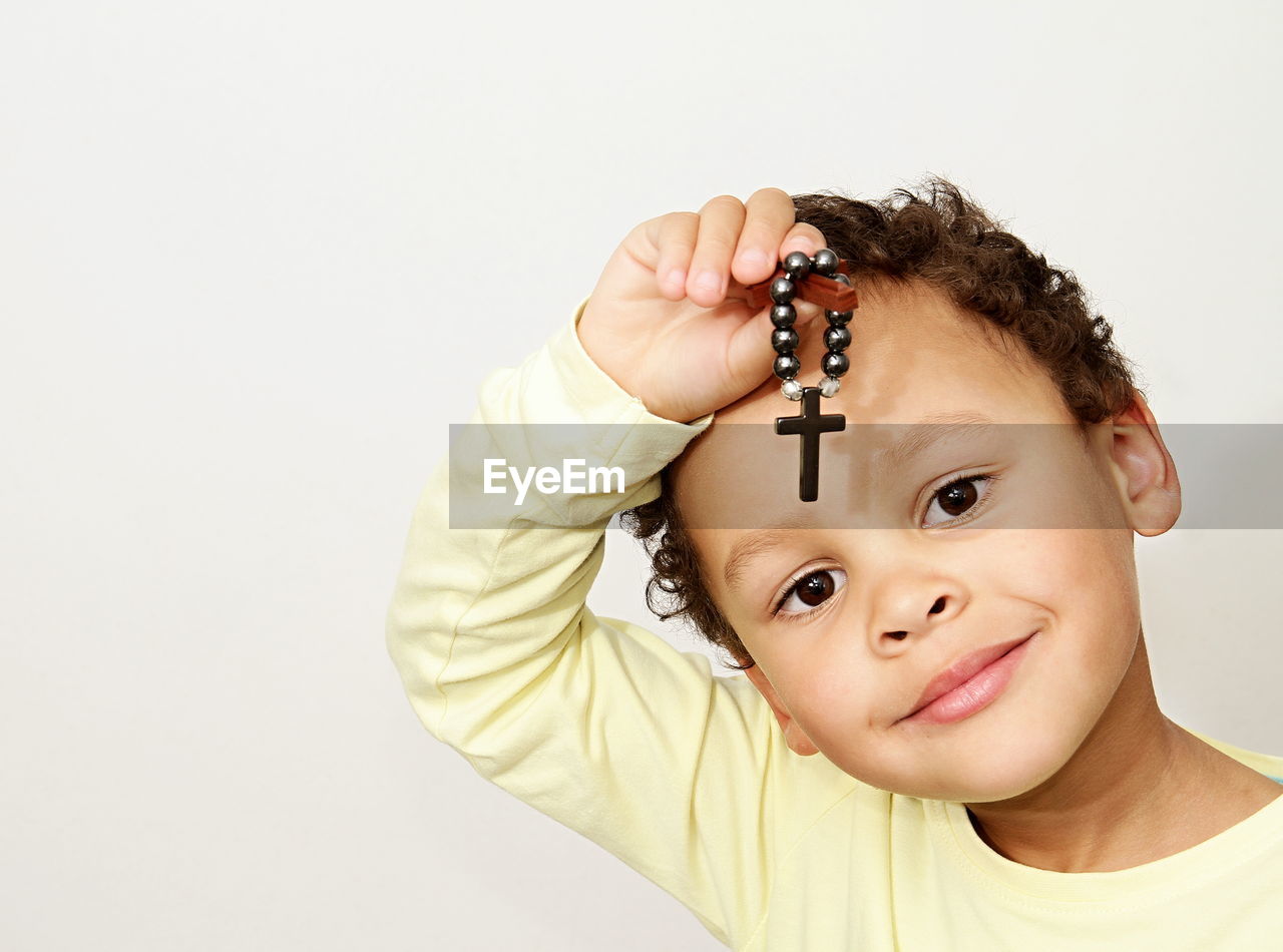 Portrait of cute boy holding cross praying against white background