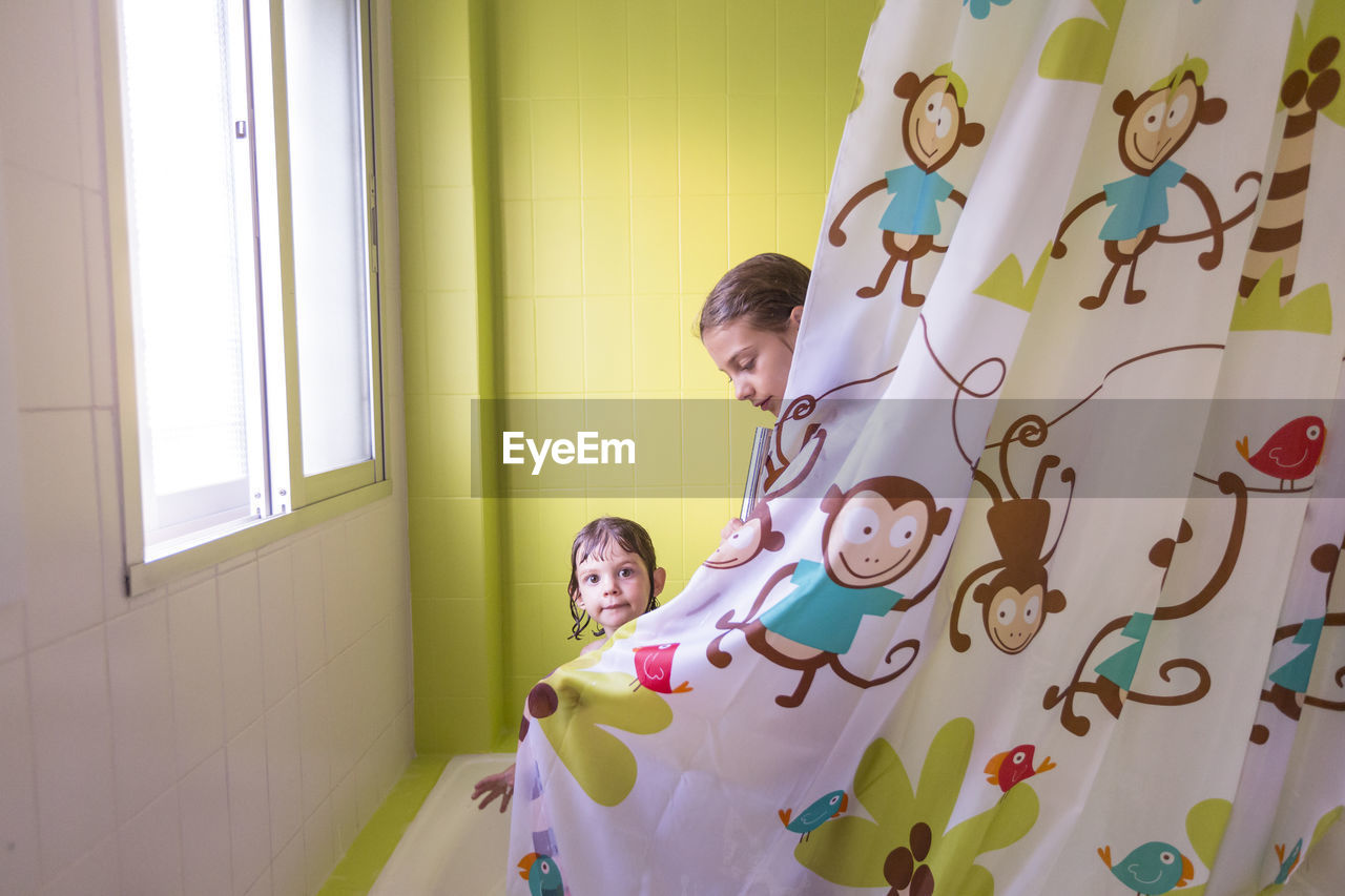 Siblings by curtain in bathtub