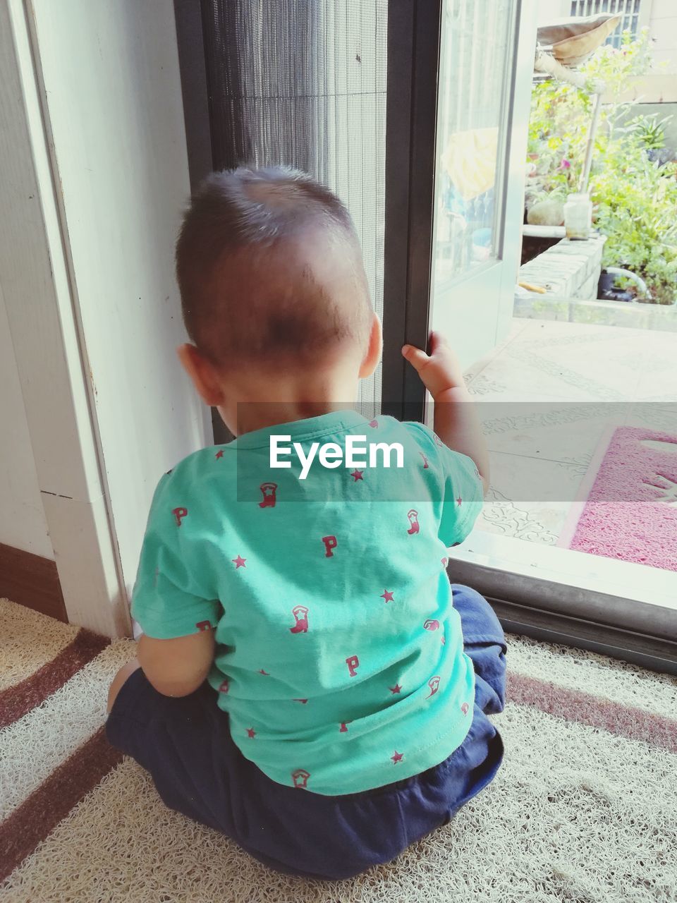 Rear view of boy sitting on rug by window at home