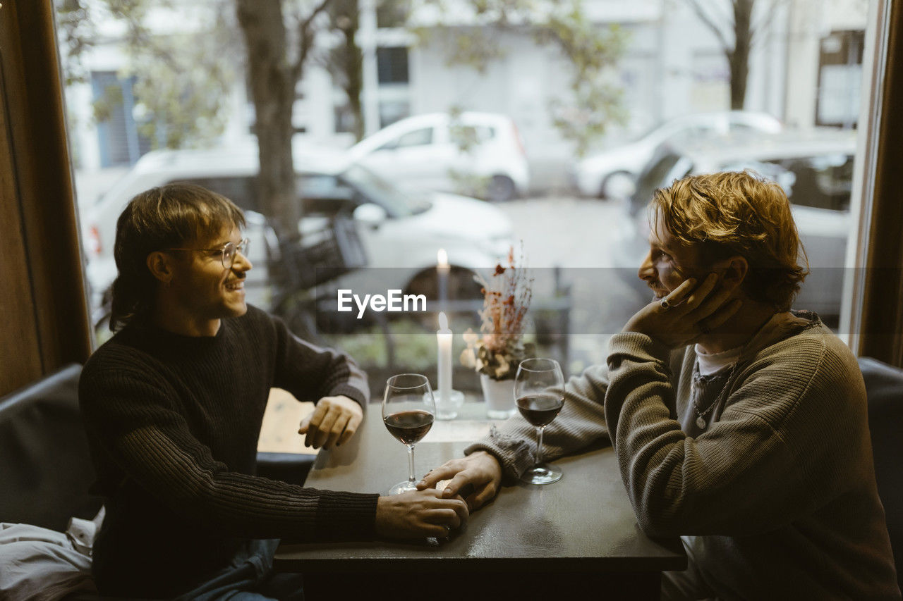 High angle view of romantic gay couple with wineglasses on table at restaurant