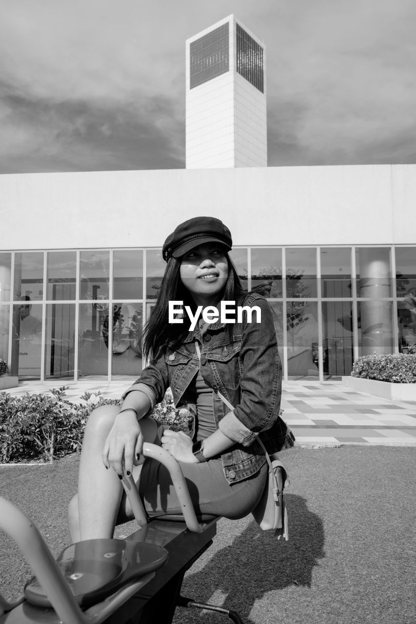 Young woman sitting against building on play equipment