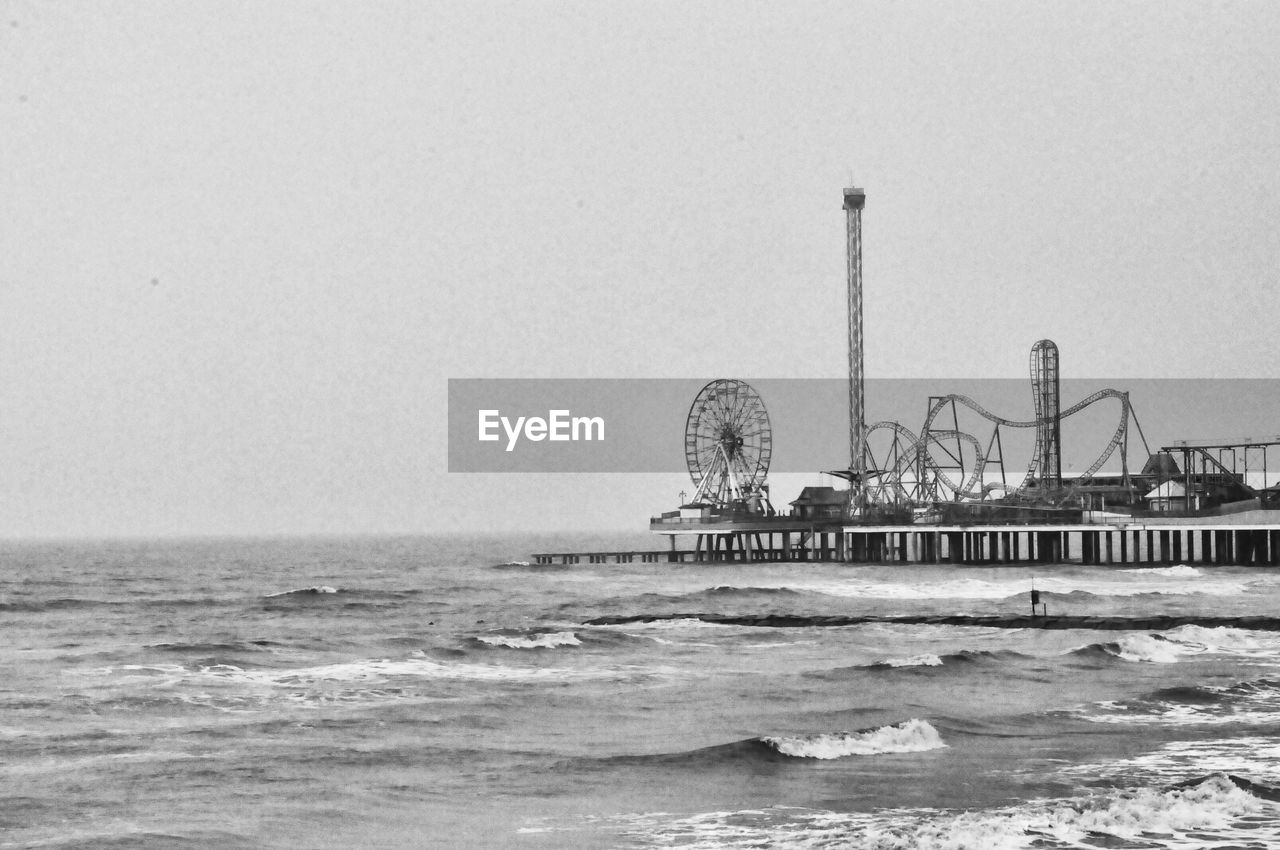 Amusement park by sea against clear sky