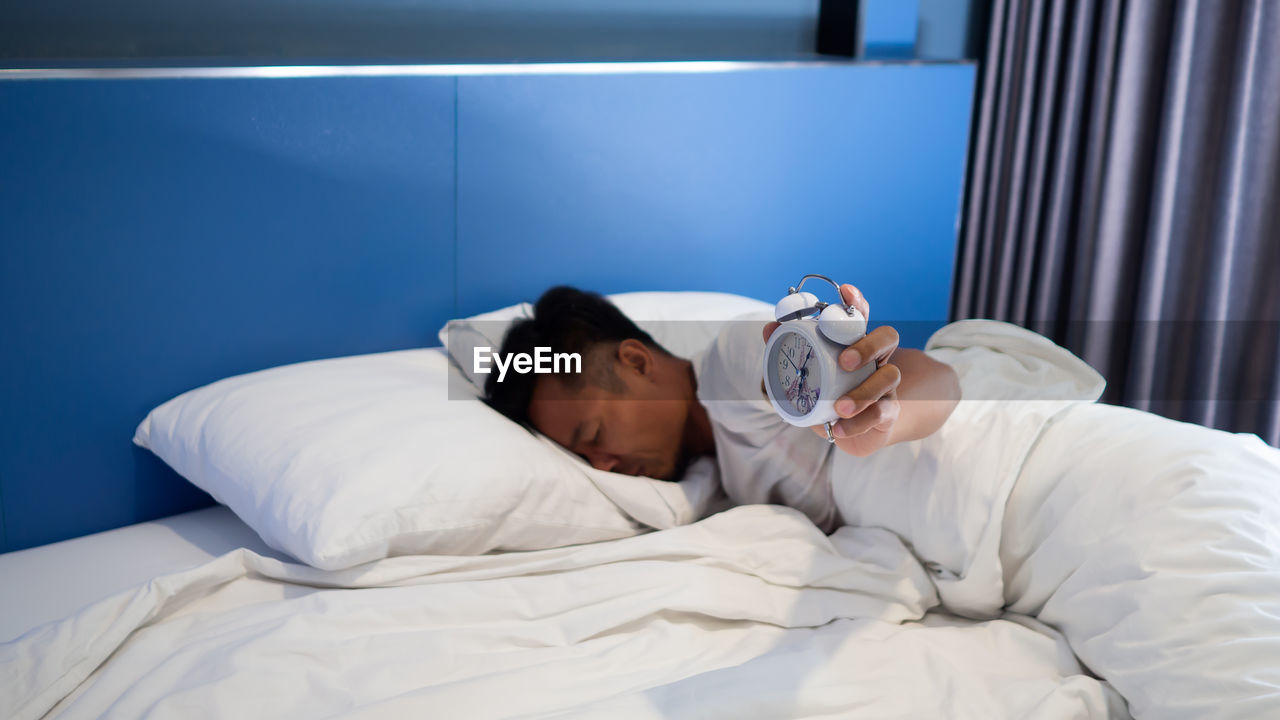 Man with alarm clock sleeping on bed at home