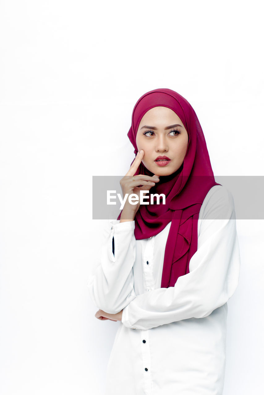 Thoughtful young woman in hijab standing against white background