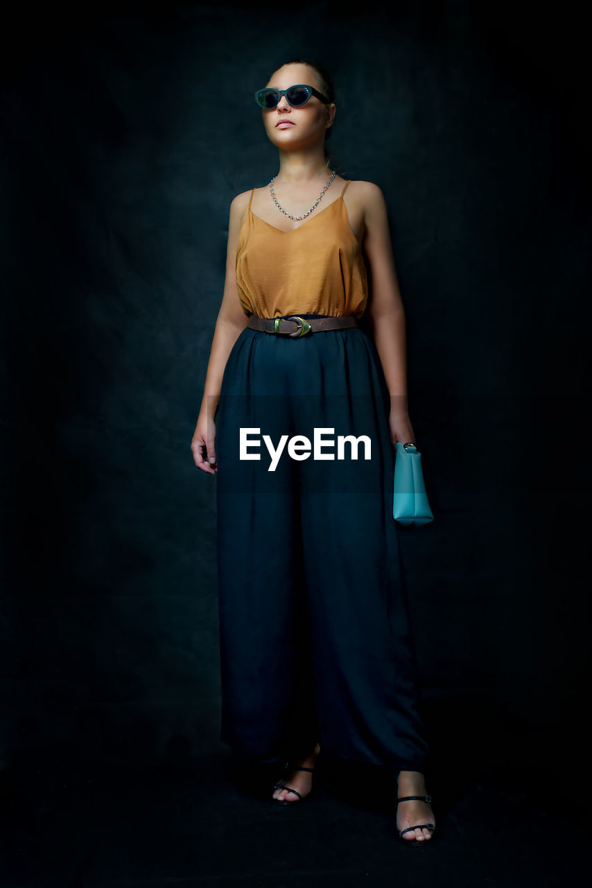 Young woman wearing sunglasses standing against black background