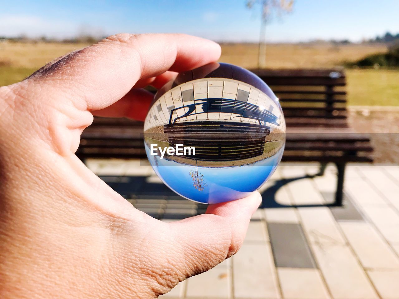 Cropped hand holding crystal ball with reflection of bench