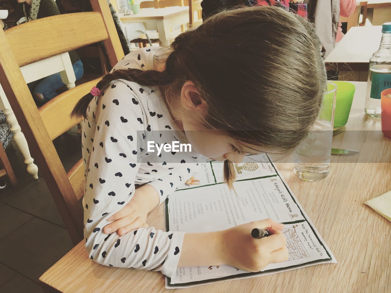 Girl drawing on page while sitting on chair at restaurant