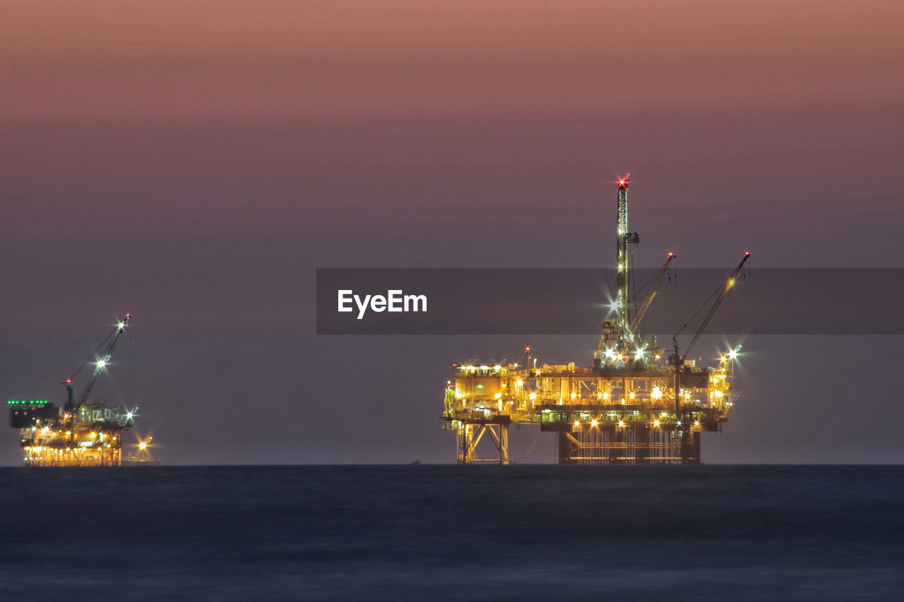 Illuminated commercial dock by sea against sky at night