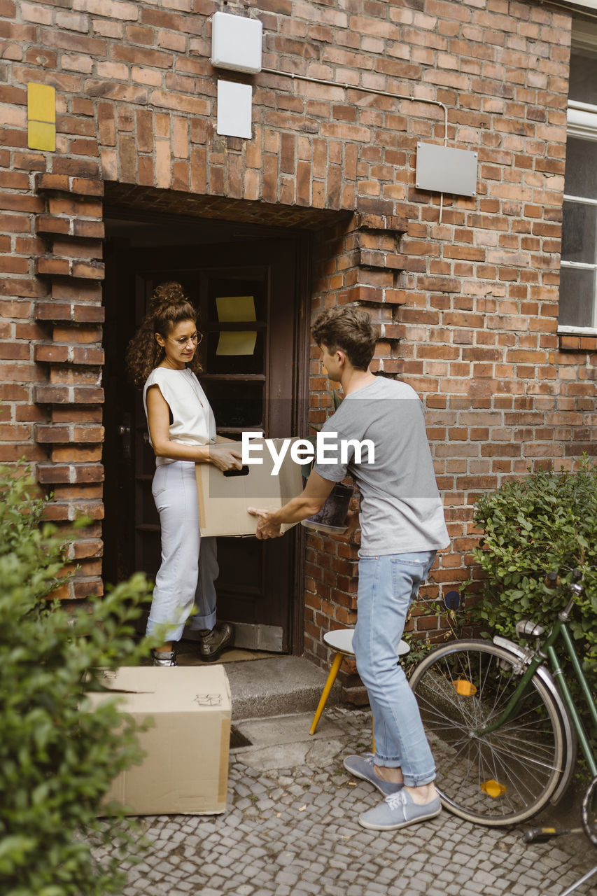 Side view of man passing cardboard box to girlfriend during relocation of house