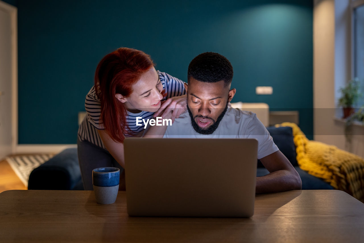 Loving young woman demanding attention from busy husband working on laptop late at home