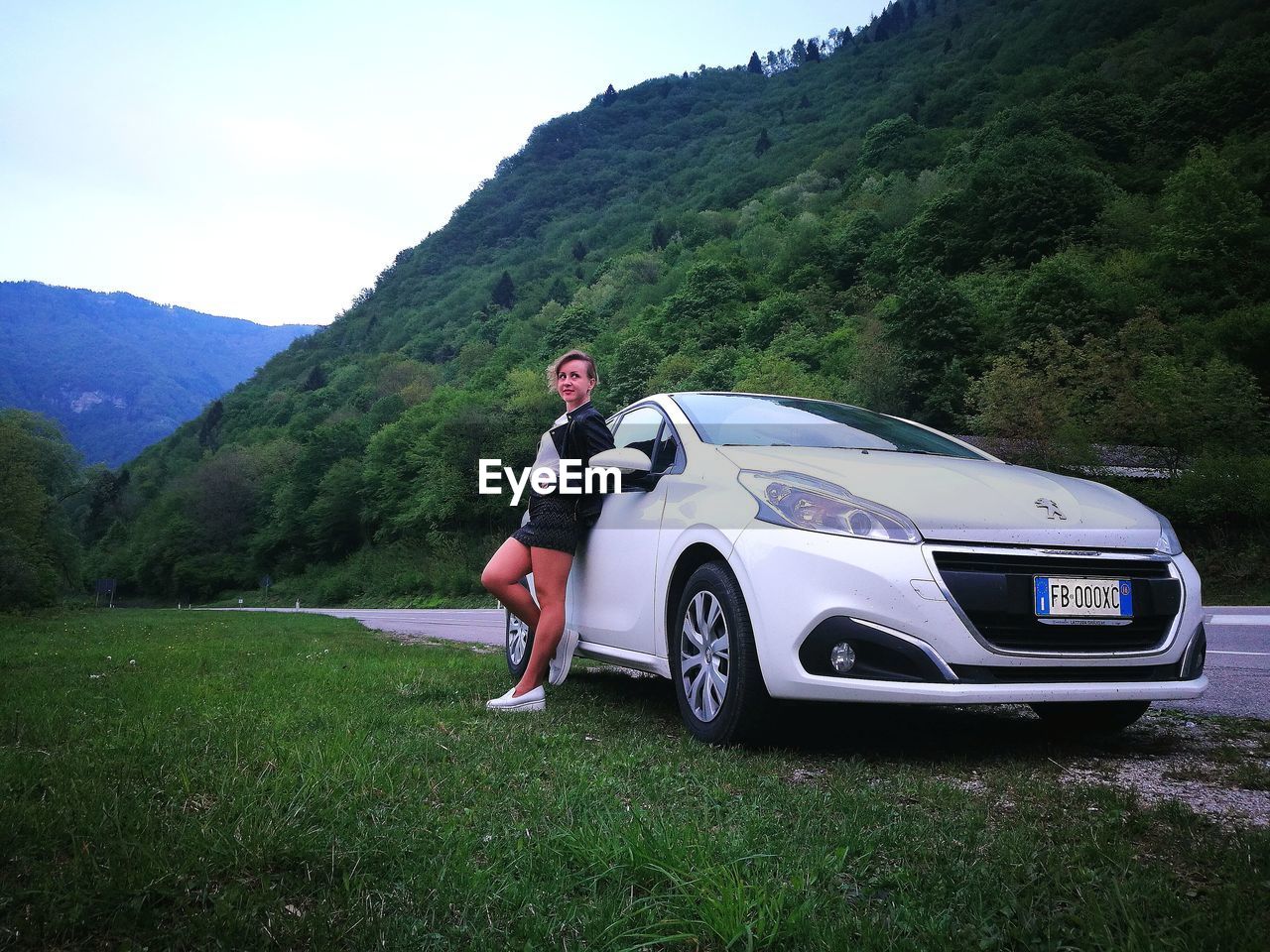 MAN STANDING ON CAR AGAINST MOUNTAIN