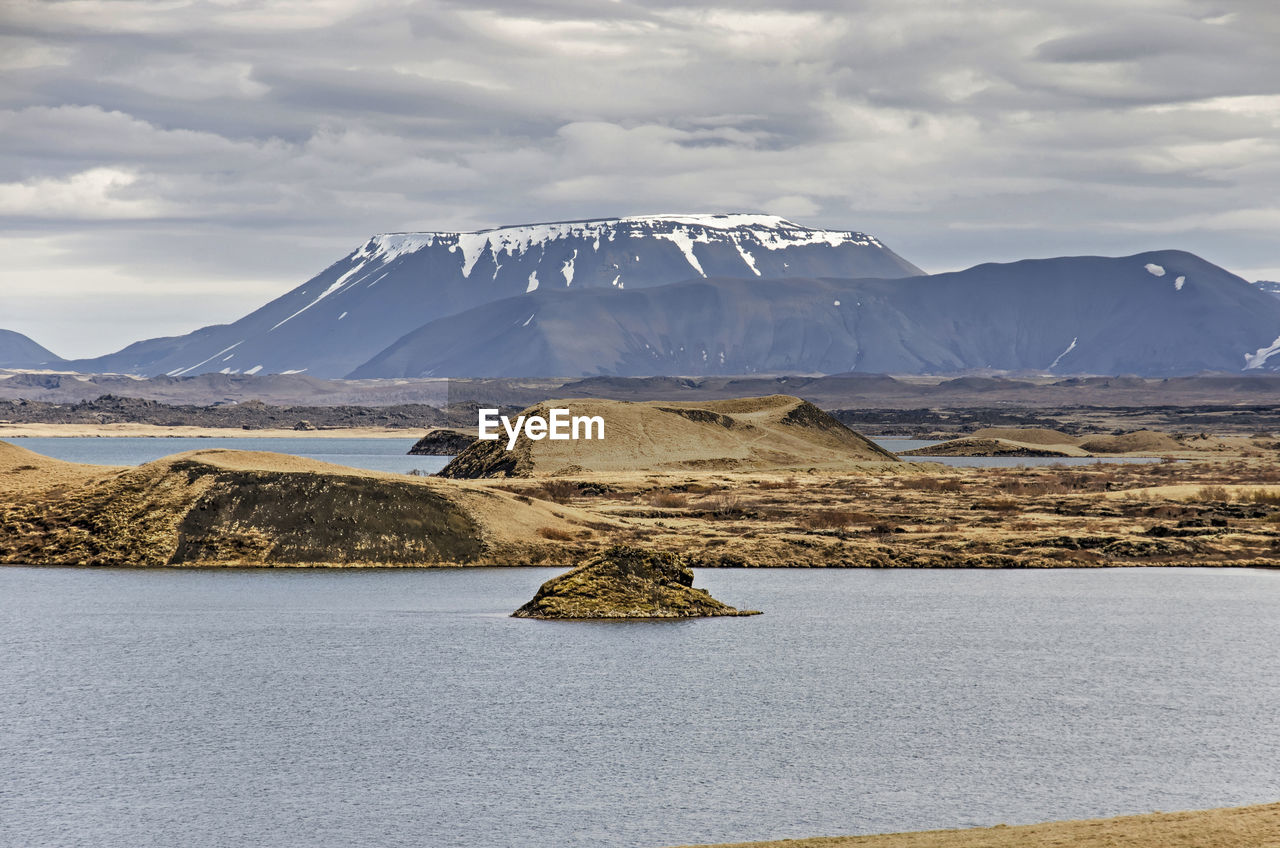 View across a lake towards a small island, a pseudocrater and a mountain range in iceland