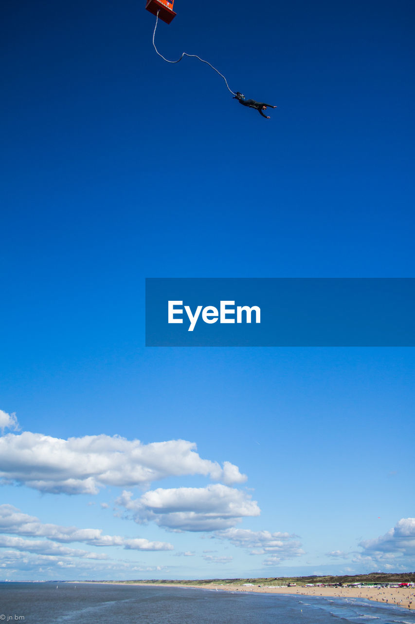 Low angle view of person bungee jumping against blue sky