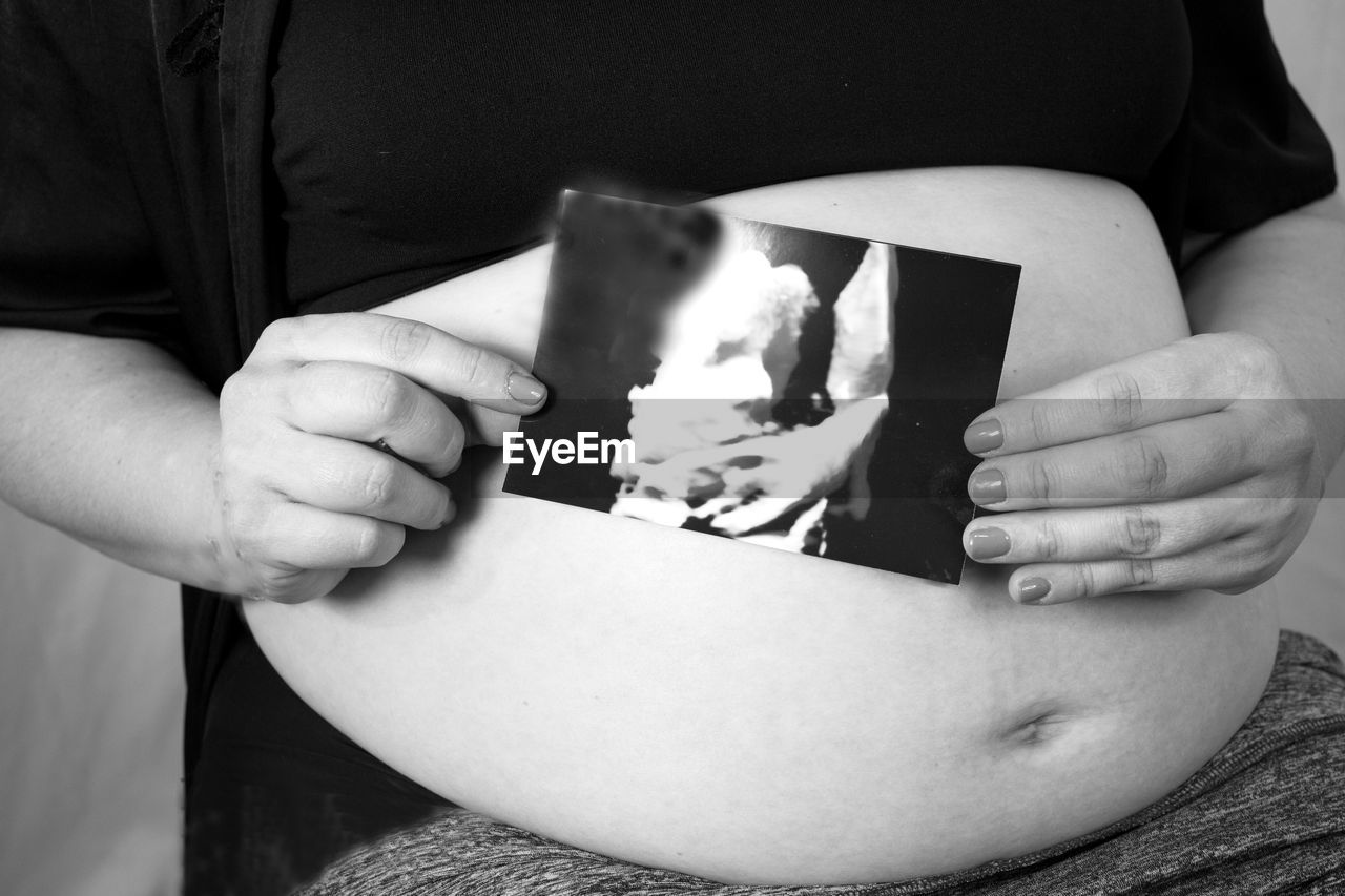 black, white, pregnant, midsection, adult, holding, black and white, parent, beginnings, person, one person, hand, women, monochrome, indoors, monochrome photography, anticipation, child, clothing, lifestyles, life events, human fertility, close-up, female, arm