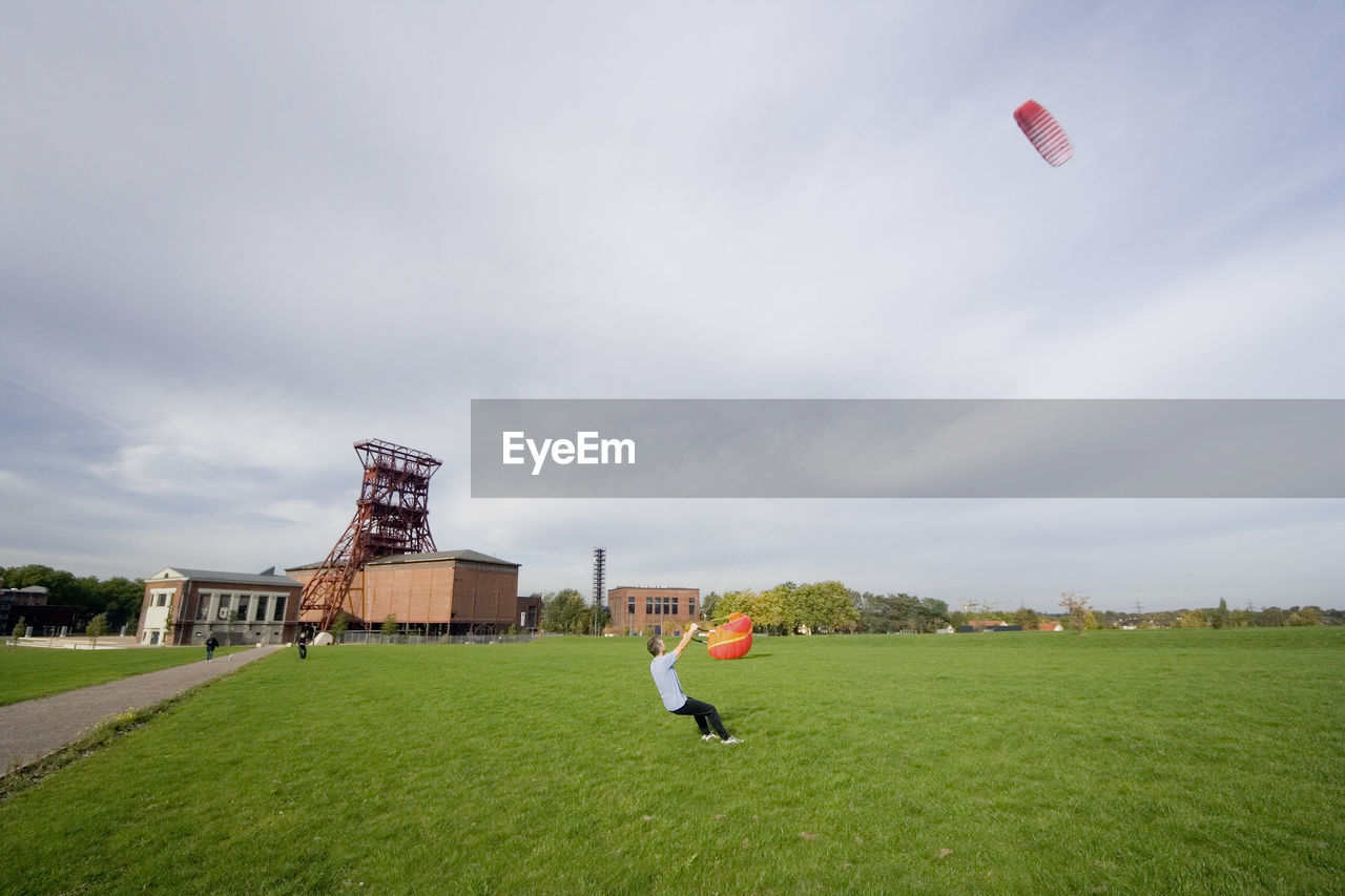 Full length of man flying kite while standing on field against cloudy sky