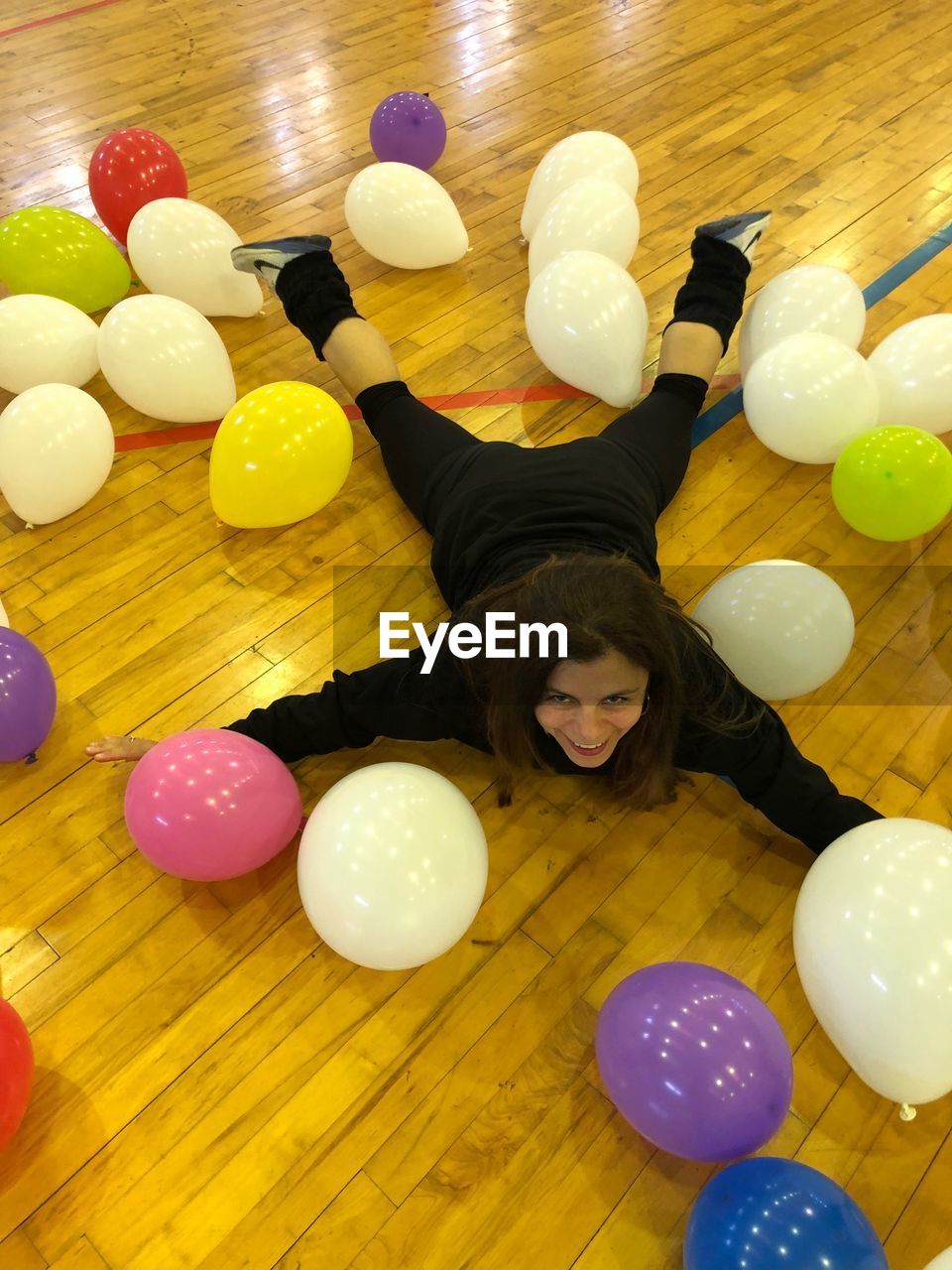 High angle view of carefree woman lying on hardwood floor amidst balloons