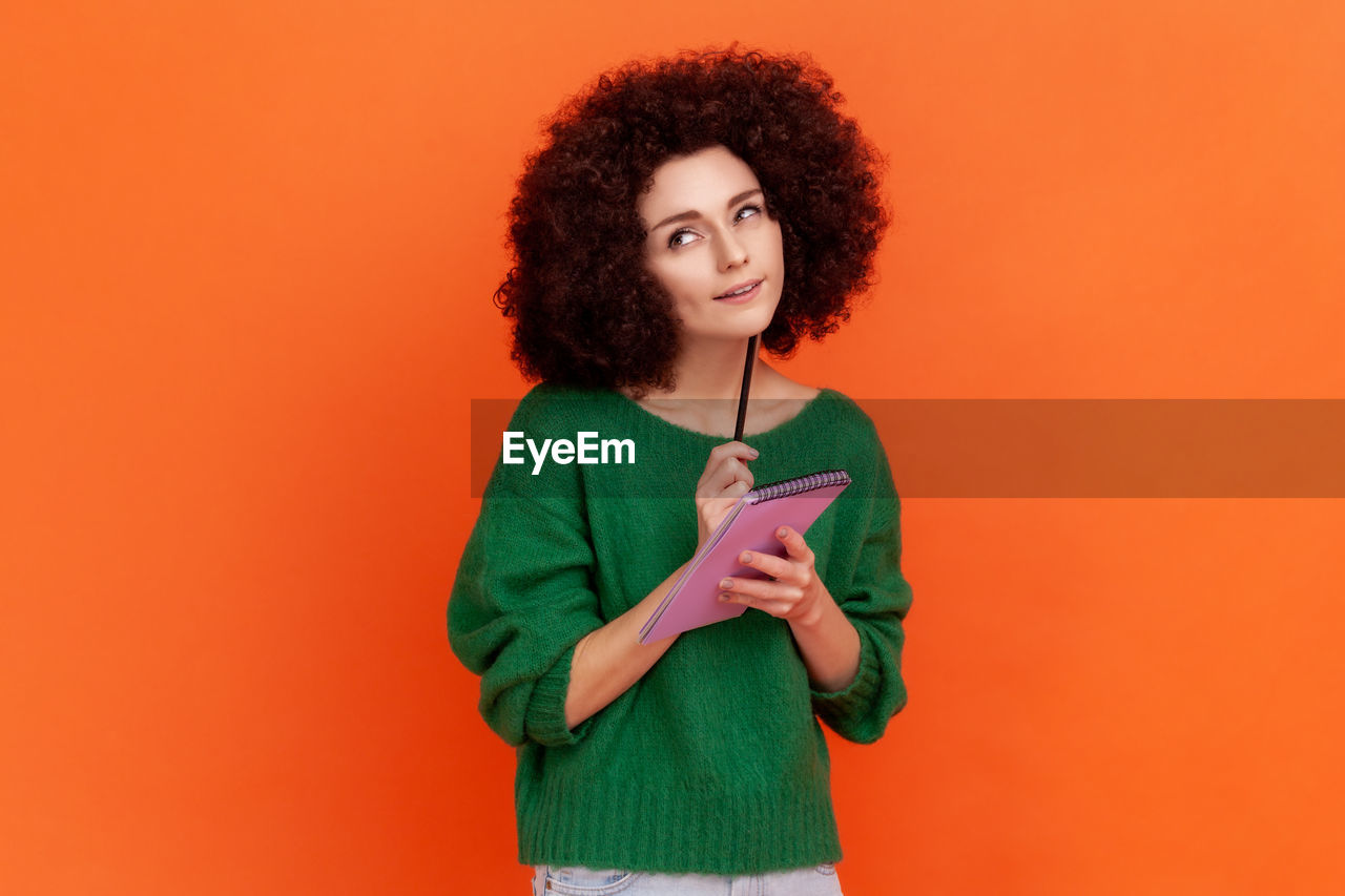 Young woman thinking while standing against colored background