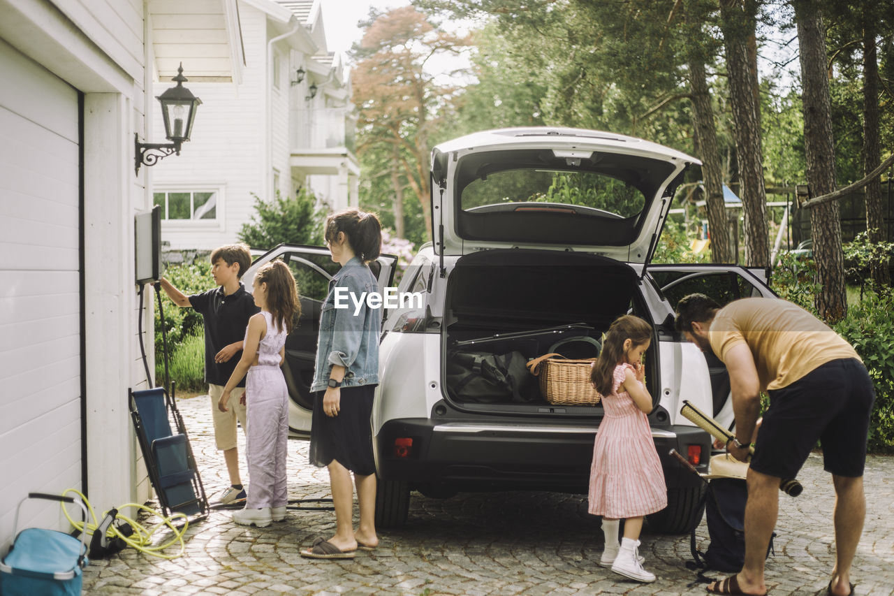 Family charging and loading luggage in trunk of electric car outside house