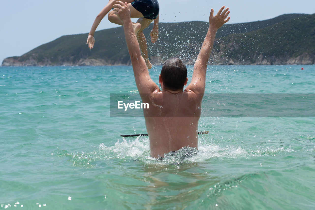 Rear view of shirtless man and boy at sea