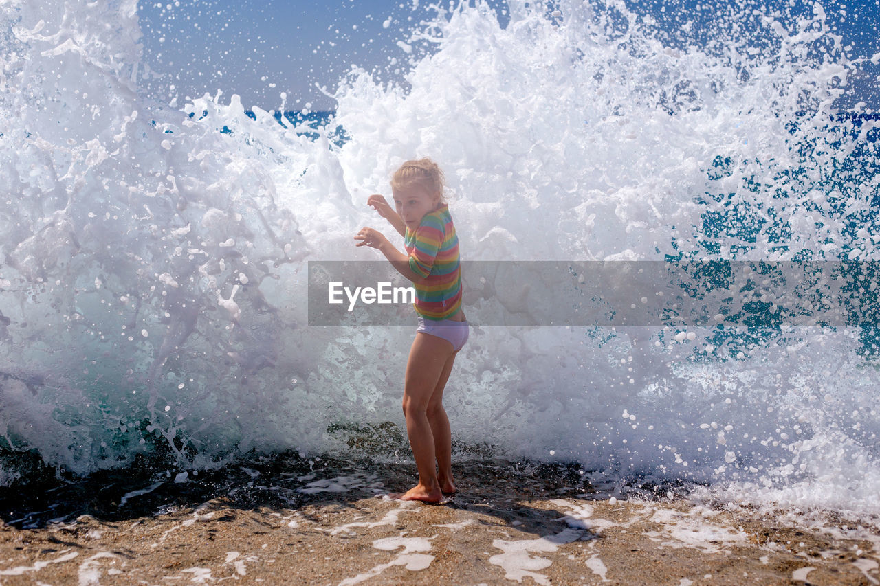 Full length of girl standing against wave