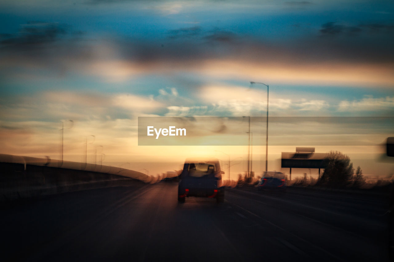 CAR MOVING ON HIGHWAY AGAINST SKY AT SUNSET