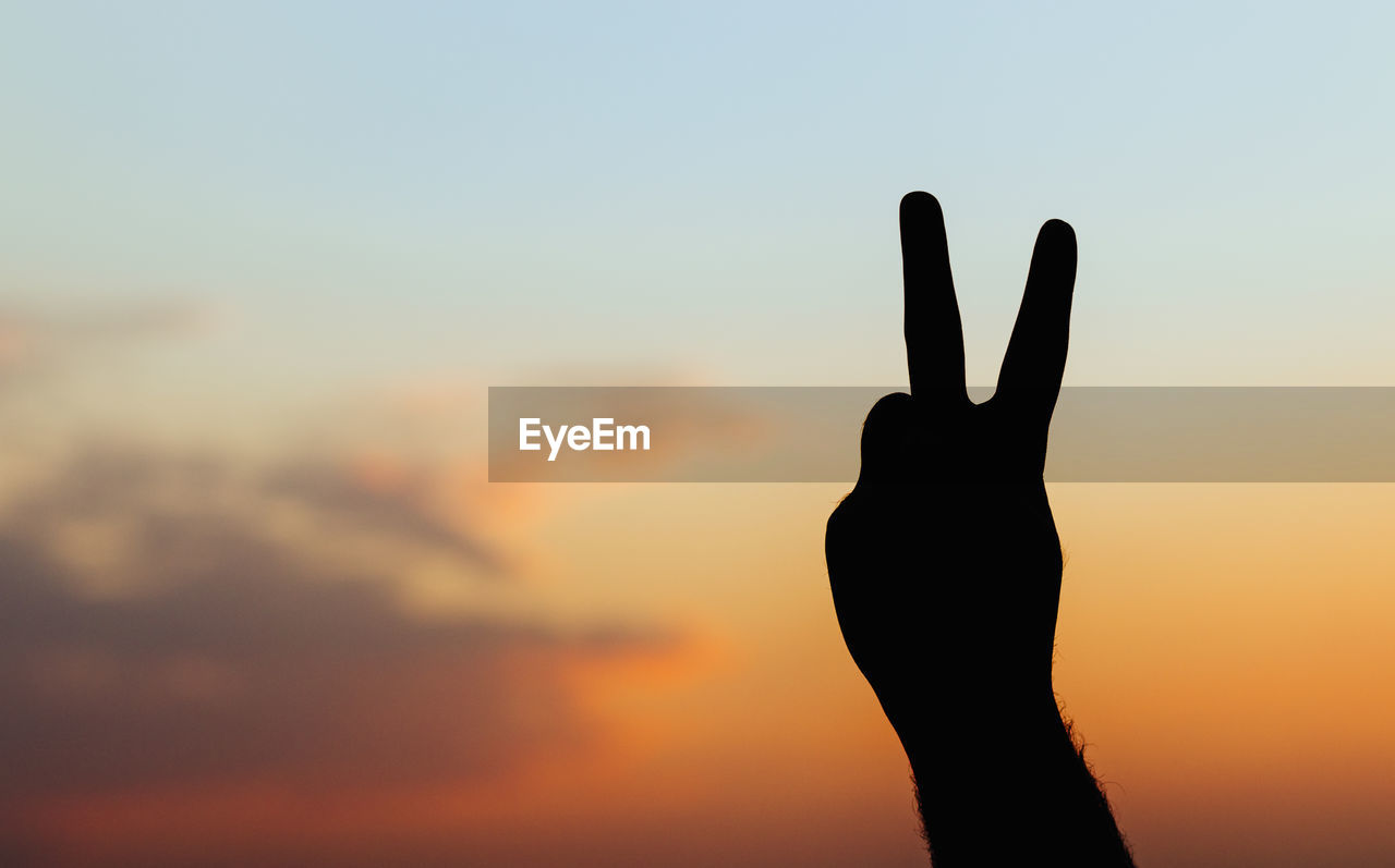 Man's hand isolated on sky background - peace gesture silhouette