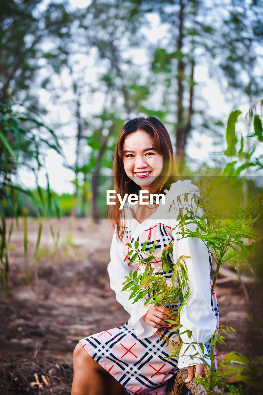 PORTRAIT OF SMILING YOUNG WOMAN SITTING ON A LAND