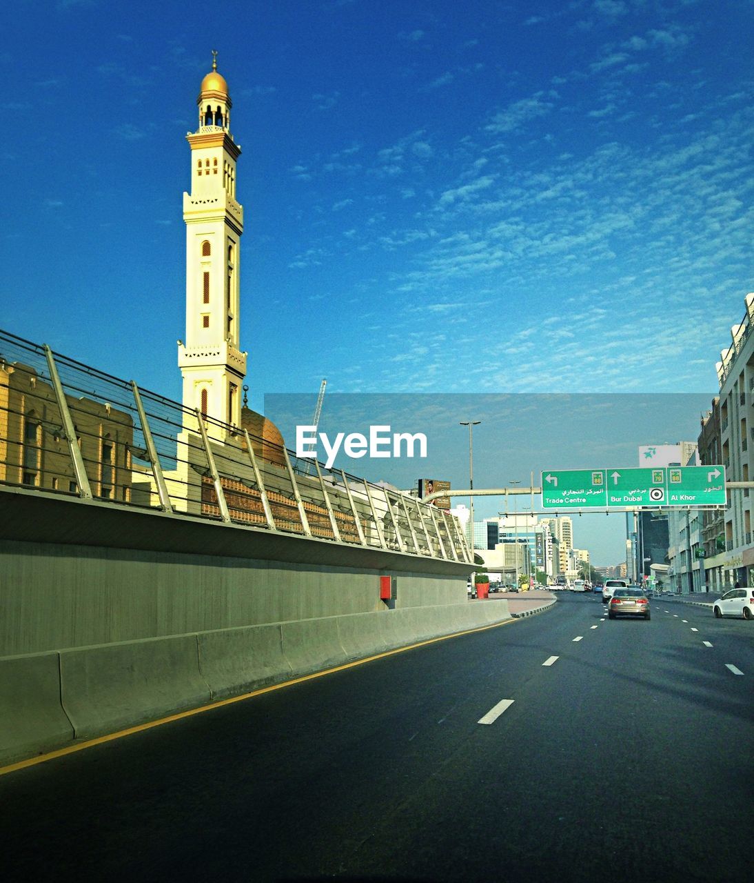 Cars moving on street by minaret against blue sky