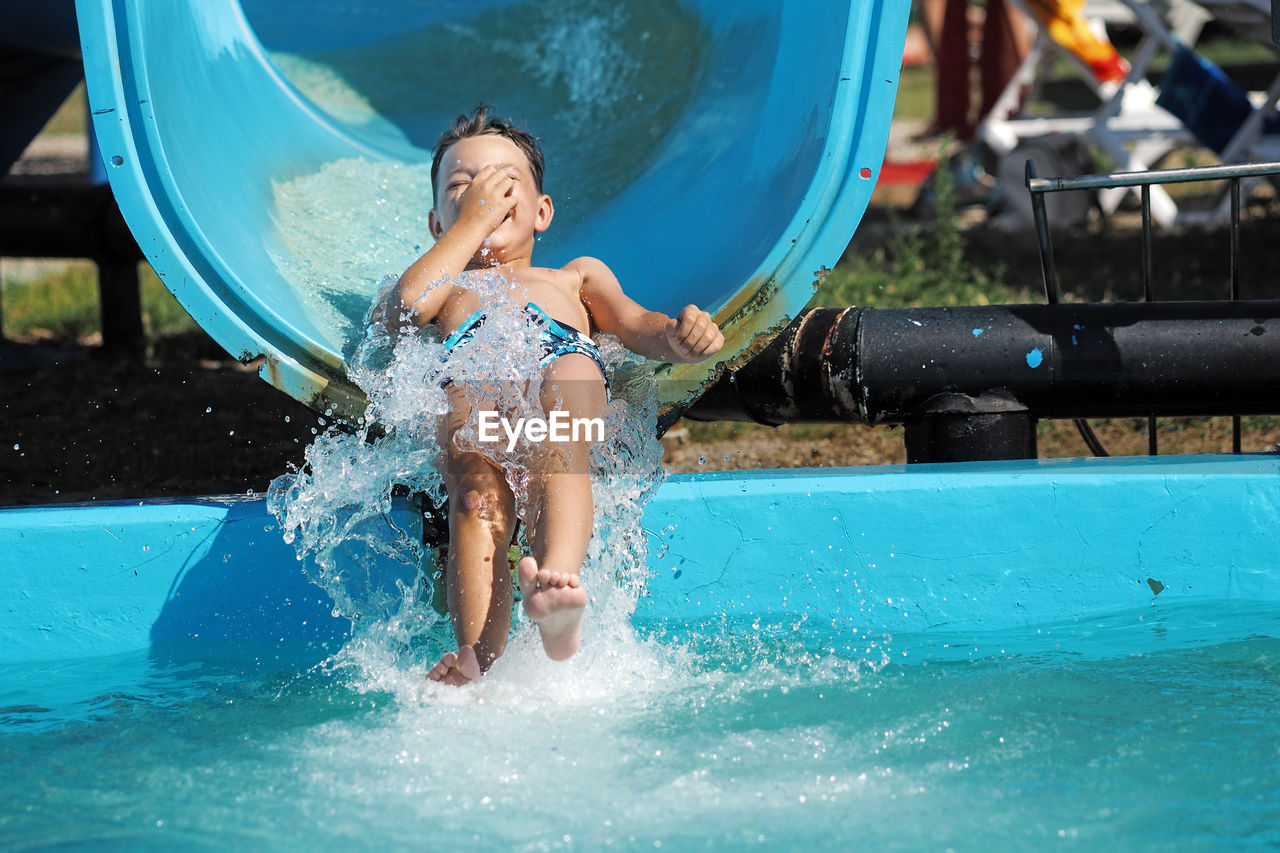 Full length of boy enjoying slide in swimming pool at water park