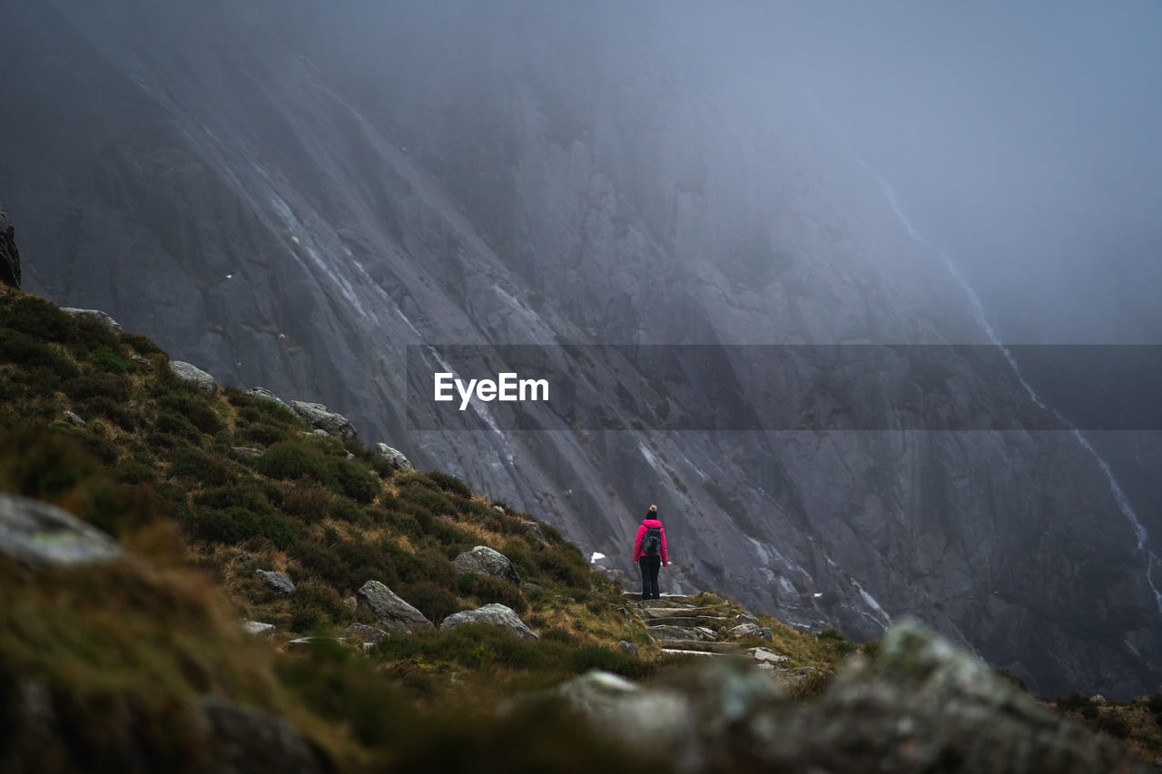 Rear view of person standing on rock against mountains