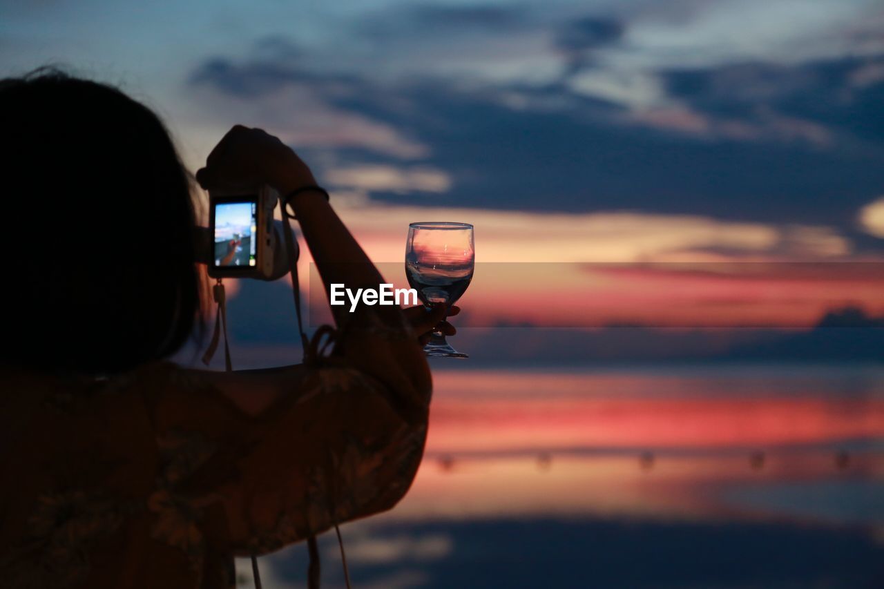 Woman photographing wineglass during sunset