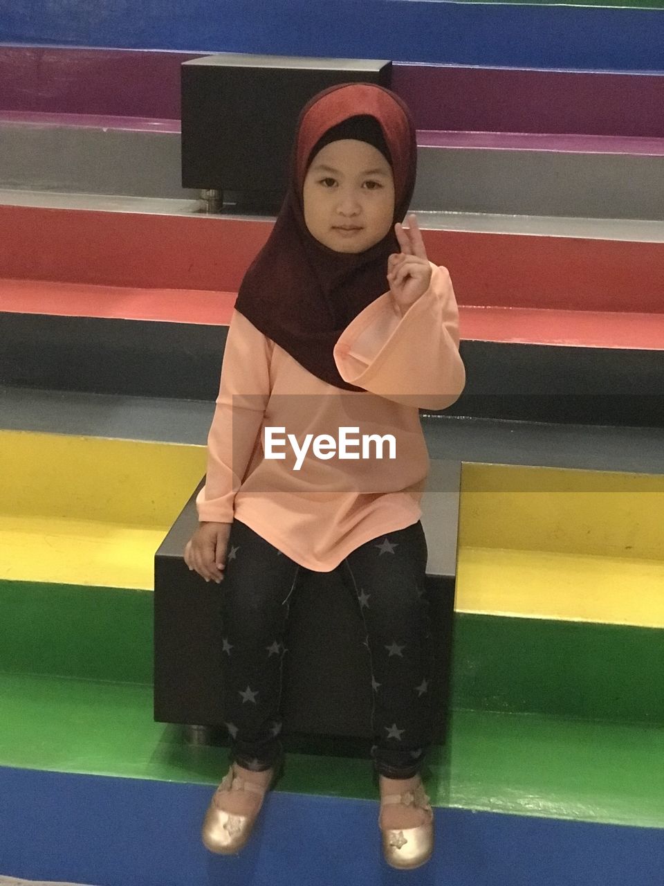 Portrait of girl wearing hijab sitting on colorful steps