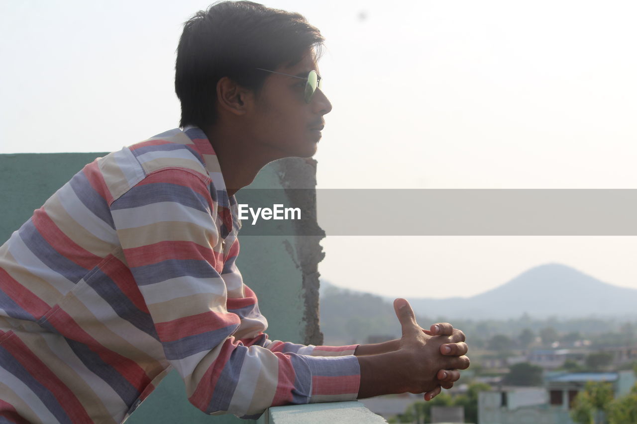 Side view of young man leaning on retaining wall at building terrace