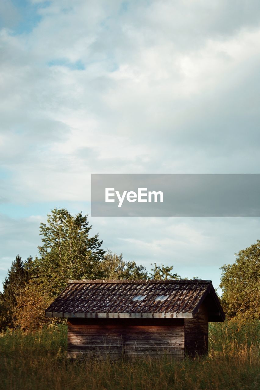 Old cabin and trees on landscape against sky