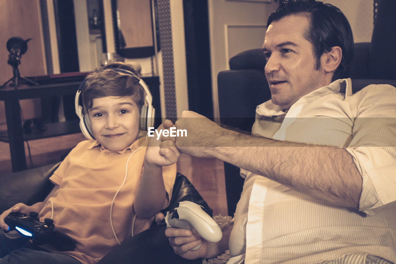 Happy boy fist bumping with his father while playing video games at home.