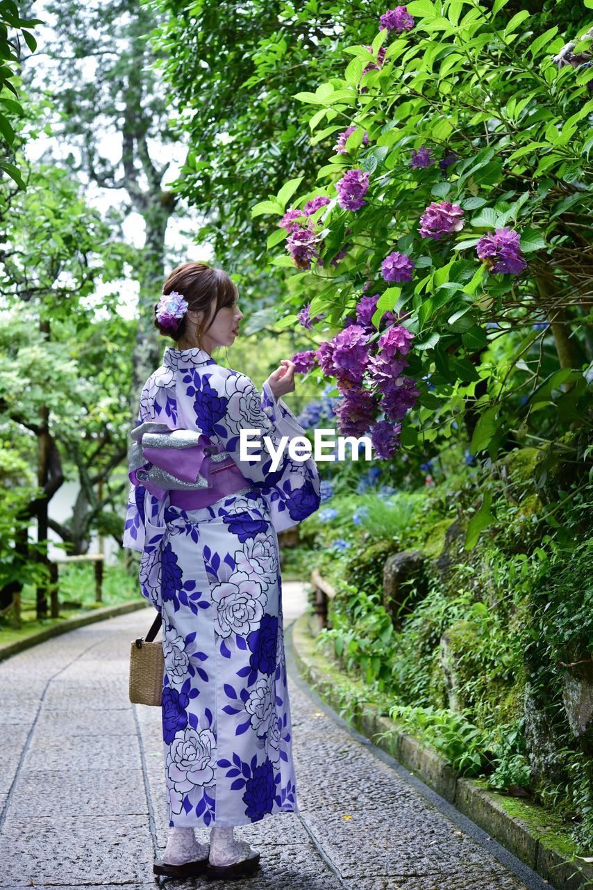 Rear view of woman standing on footpath by flowering plants