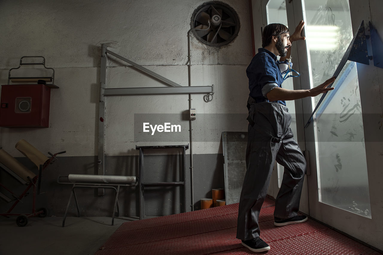 Side view of man looking through door in factory