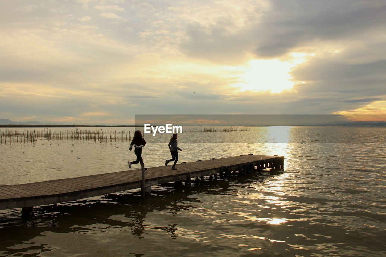 SILHOUETTE PEOPLE ON PIER OVER SEA AGAINST SKY