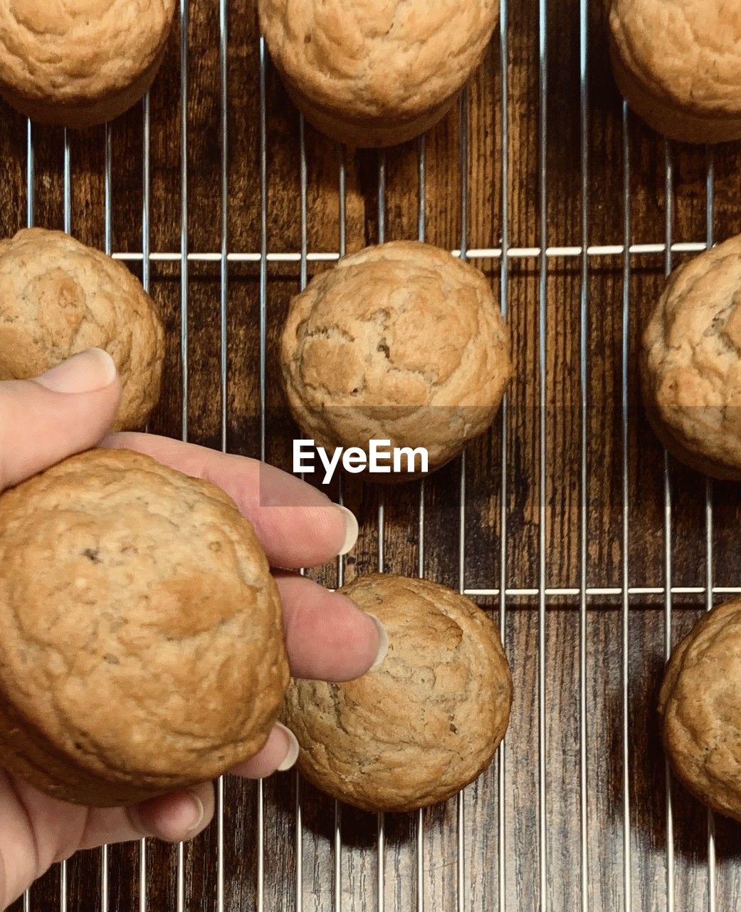 Baked muffins on a rack and hand holding one muffin