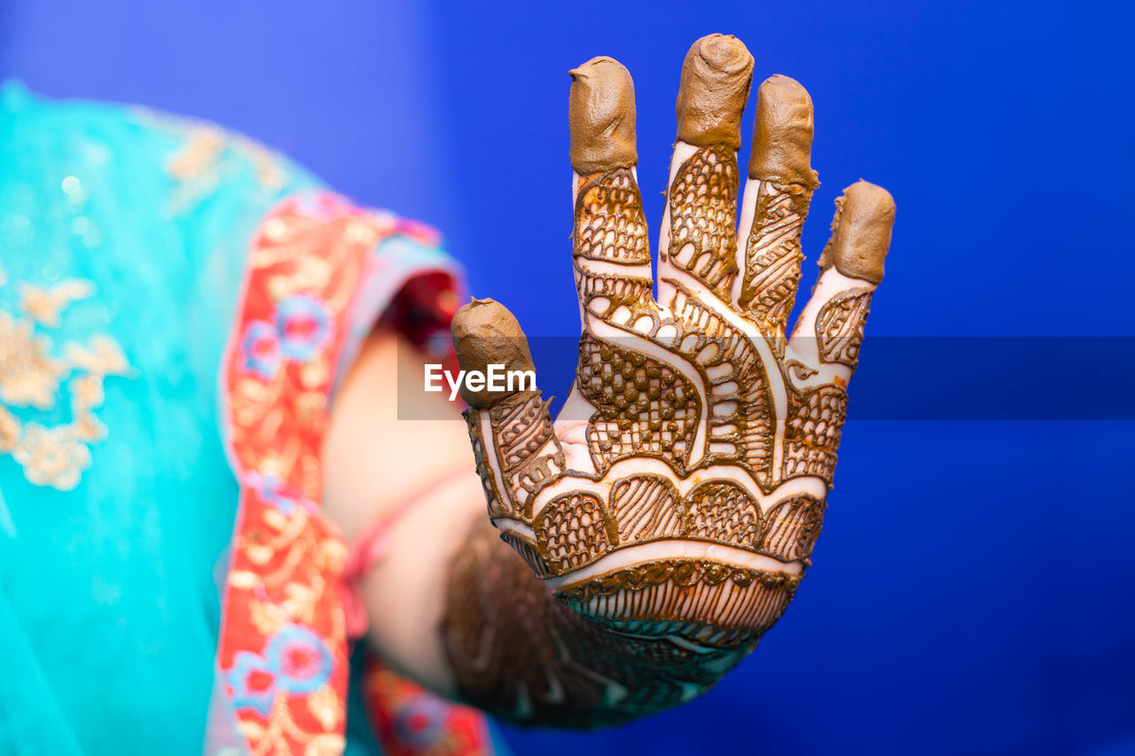 Midsection of bride with henna tattoo against blue background