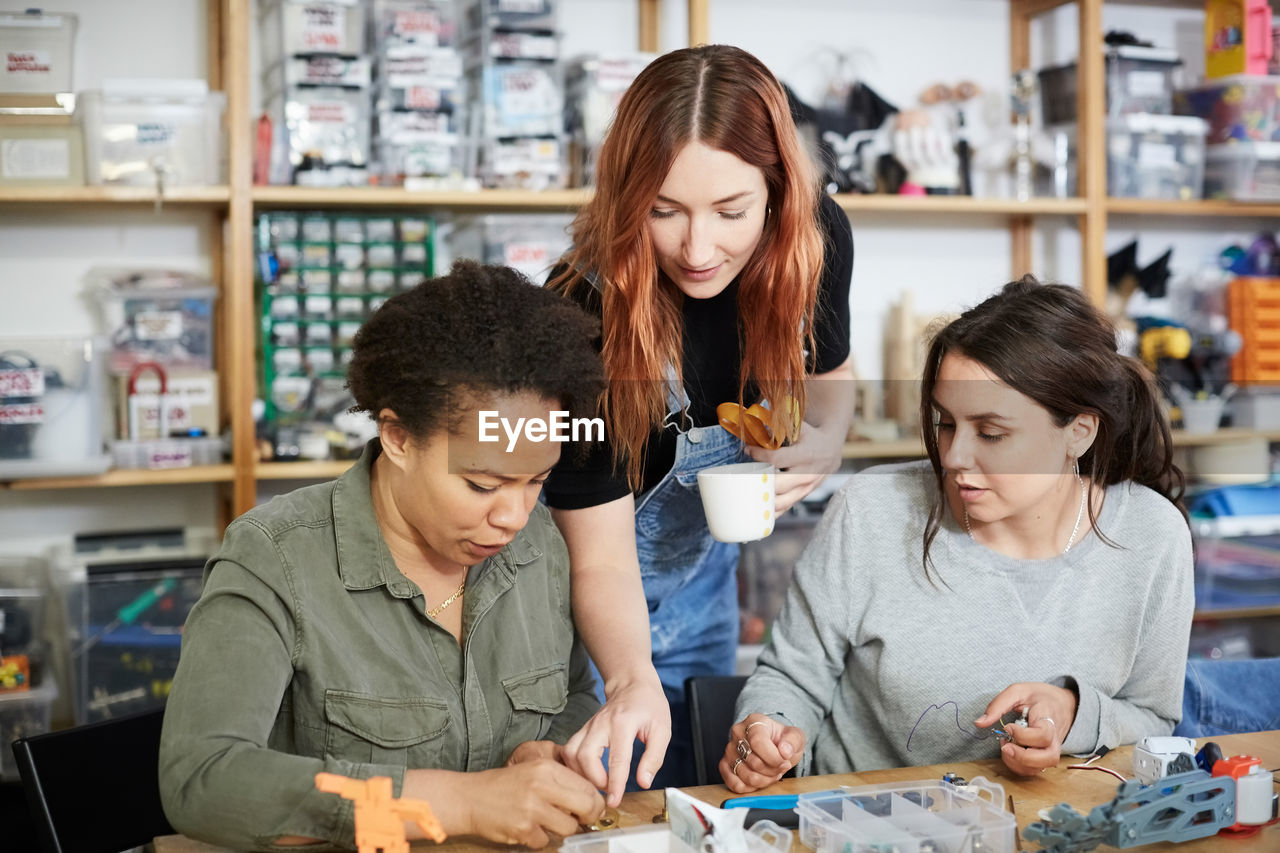 Redhead technician pointing to female coworkers at workshop