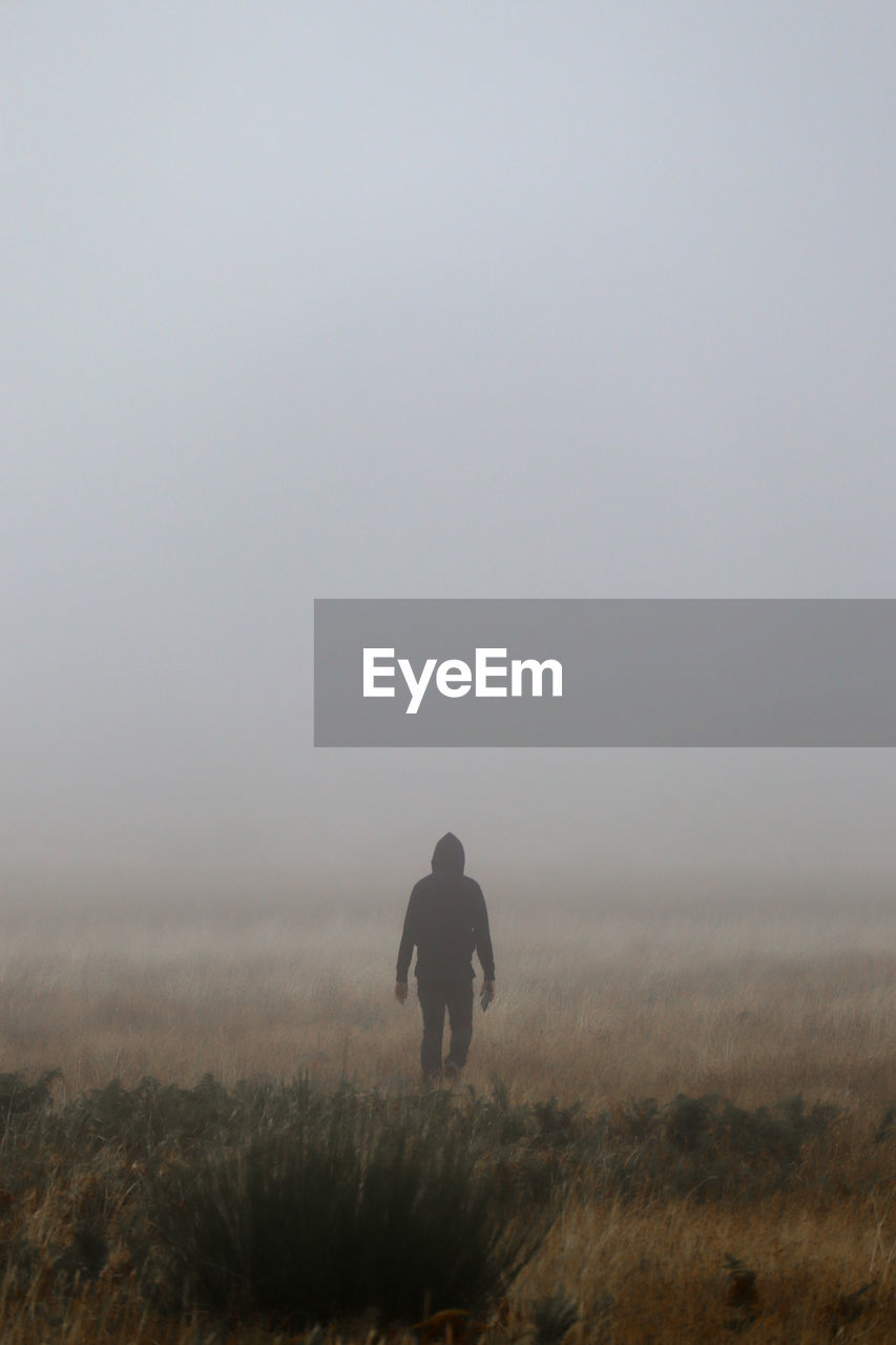 Rear view of man walking on field against clear sky