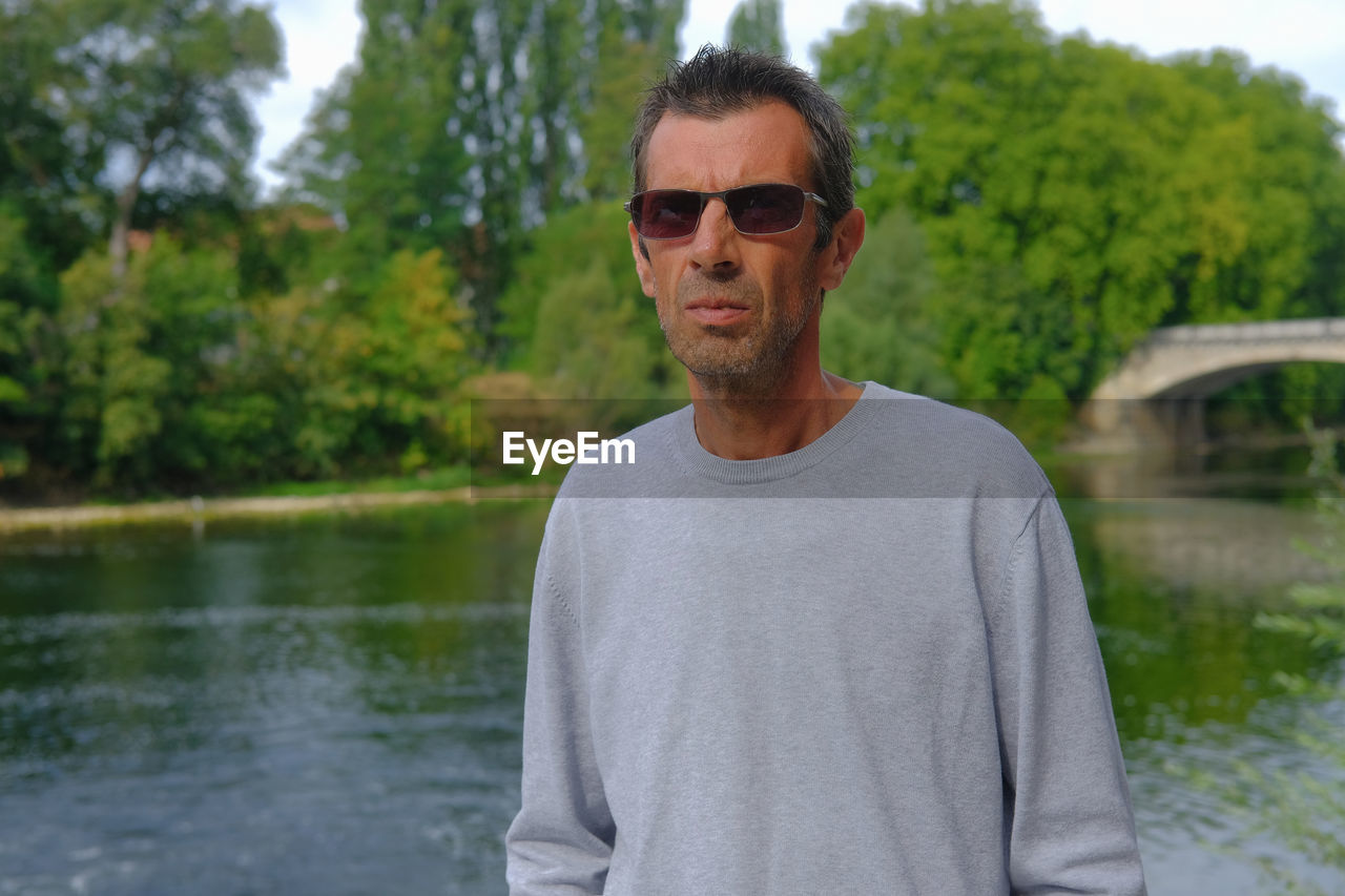 Portrait of man standing by lake against trees