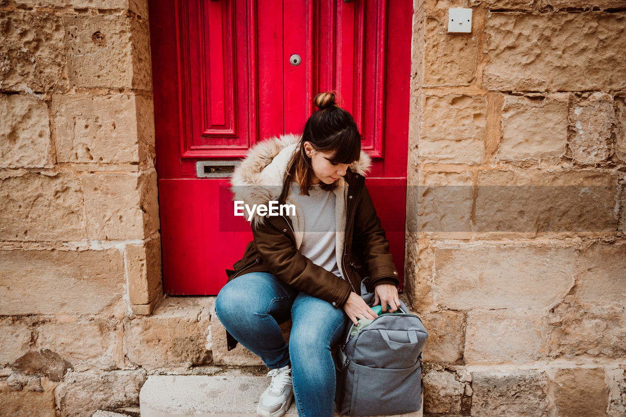 Full length of woman with backpack sitting by door